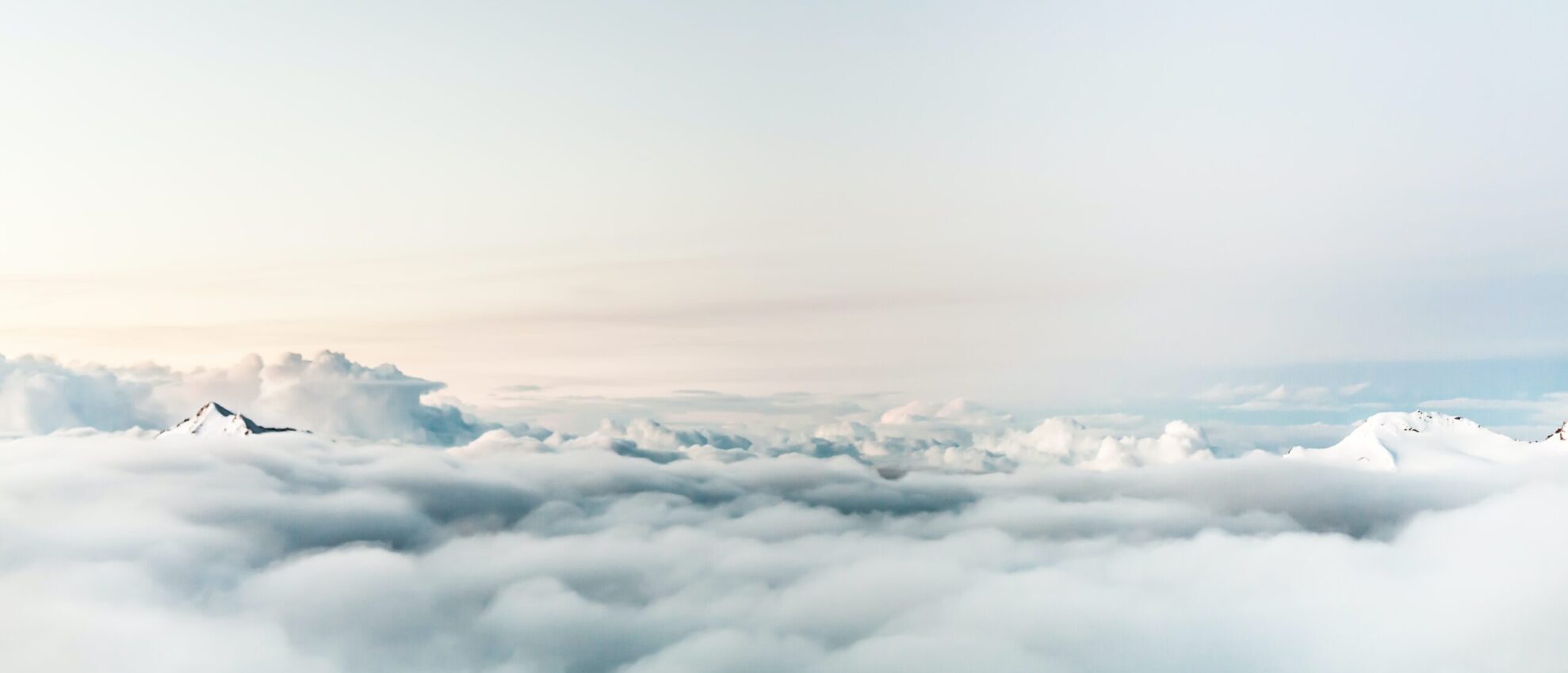 Ausblick über eine dichte Schicht aus weißen Wolken. Eine schneebedeckte Bergspitze ragt durch die Wolkendecke hindurch.