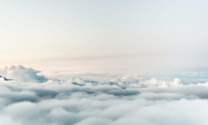 Ausblick über eine dichte Schicht aus weißen Wolken. Eine schneebedeckte Bergspitze ragt durch die Wolkendecke hindurch.